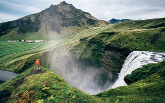 Hiker overlooking the top of Skogafoss Waterfall and green cliffs on Iceland’s South Coast.