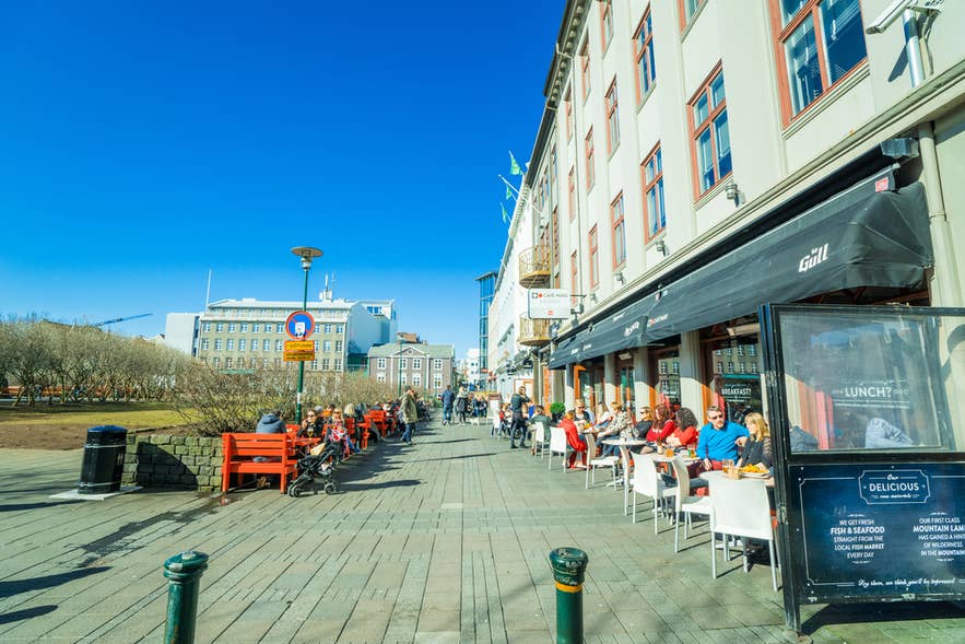 Persone che pranzano all'aperto in una via soleggiata di Reykjavik, tipica atmosfera di aprile nel centro città.