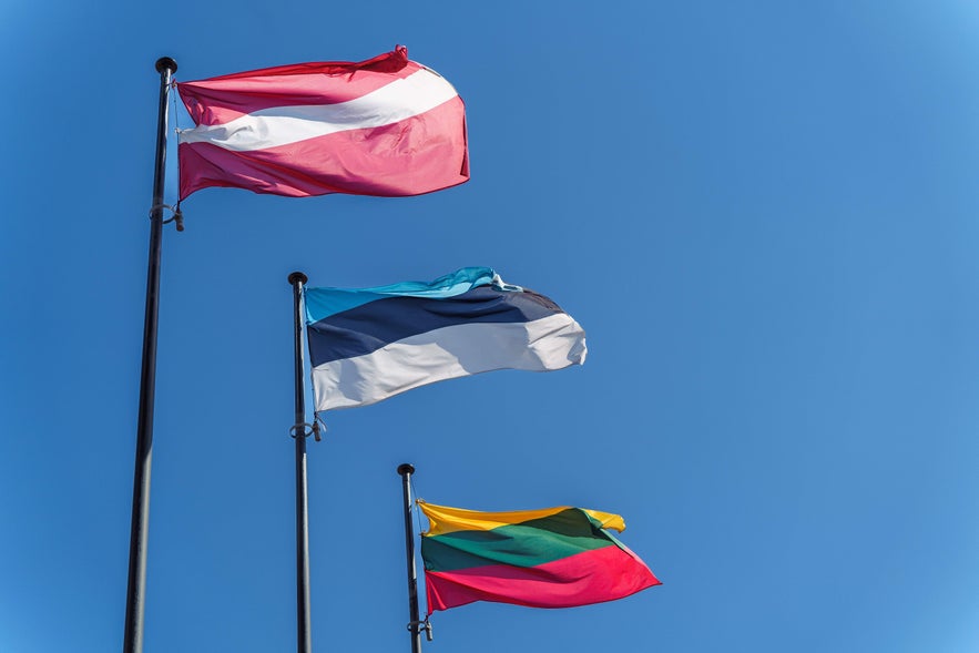 Flags of Estonia, Latvia, and Lithuania waving against a blue sky, representing Iceland as the first country to recognize Baltic independence in 1991.