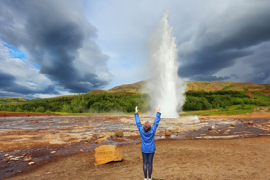 Traveler cheering as Strokkur Geyser erupts in the Geysir Geothermal Area, a must-see in Iceland in April.