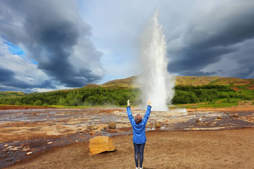Viaggiatore che esulta mentre il geyser Strokkur erutta nell’area geotermica di Geysir, una tappa imperdibile in Islanda ad aprile.