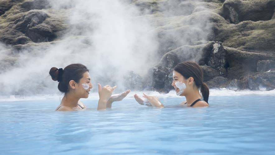 Two people relaxing in the Blue Lagoon in Iceland wearing silica mud masks, showing the iconic spa skincare experience.