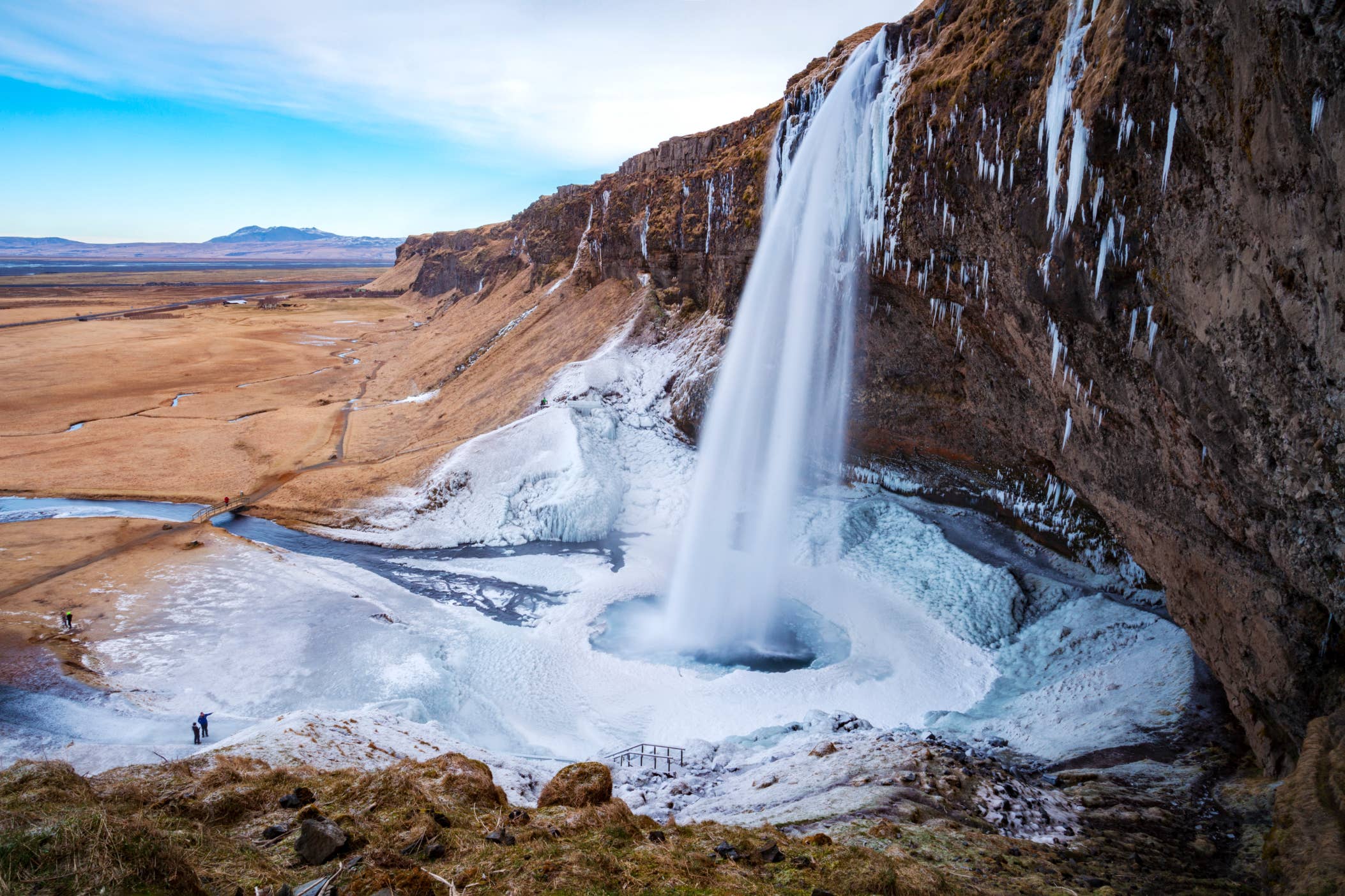 Seljalandsfoss waterfall with brown cliffs and icy river in winter in Iceland.