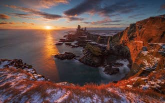 Golden winter sunset over the Londrangar Sea Cliffs and rock stacks on the Snaefellsnes Peninsula in West Iceland.