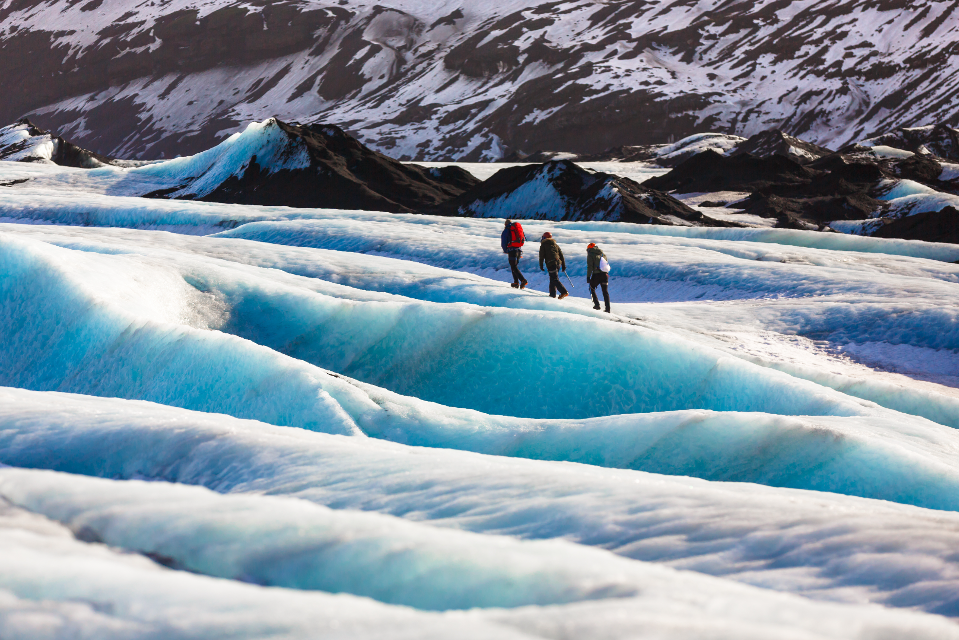 Travelers walking on the blue ice formations of Solheimajokull Glacier.