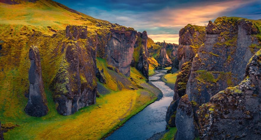 Sunset casts warm light over Fjadrargljufur canyon and winding river in South Iceland’s mossy cliffs.