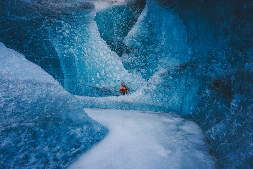 Explorer in red gear stands inside a stunning blue ice cave at Vatnajokull Glacier in Iceland.