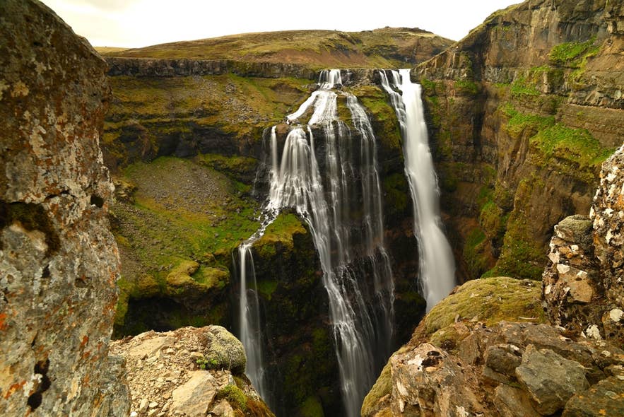 Der Glymur stürzt durch eine steile, moosige Schlucht in Island, sein mehrstufiger Fall eingerahmt von schroffen Klippen.