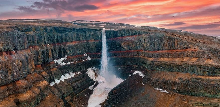 La cascata Hengifoss scende lungo scogliere di basalto striate di rosso nell’Islanda orientale, illuminata da un vivido cielo al tramonto.