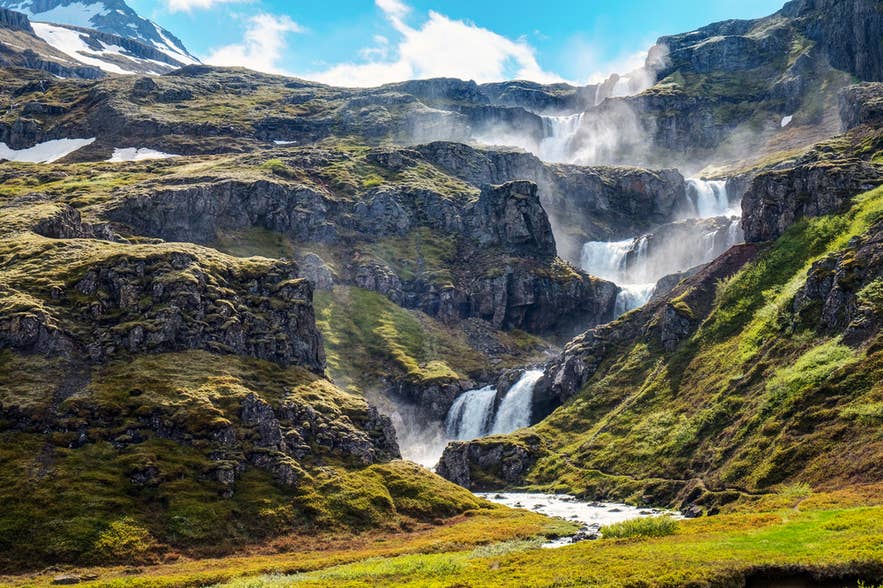 La cascata Klifbrekkufossar scende lungo pareti a gradoni nell’Islanda orientale, circondata da valli verdi e pendii rocciosi.