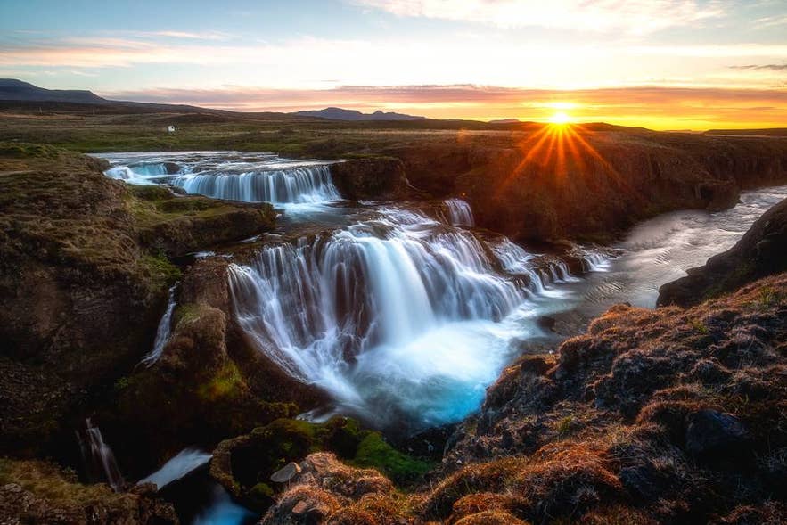 Der Reykjafoss-Wasserfall leuchtet im Sonnenuntergang in Nordisland; er stürzt über moosbedeckte Felsen in ein wildes, goldfarbenes Tal.