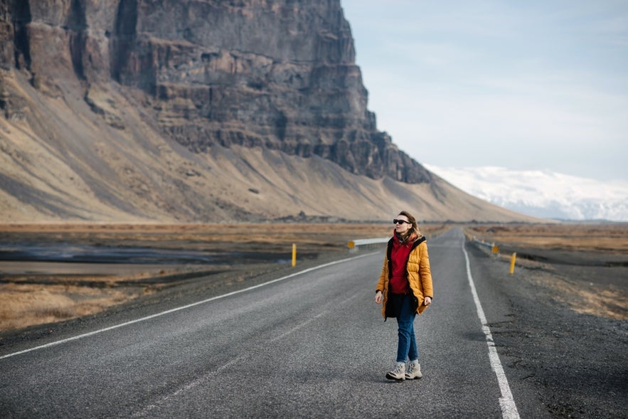 A woman wearing winter clothing walks down a road in Iceland.