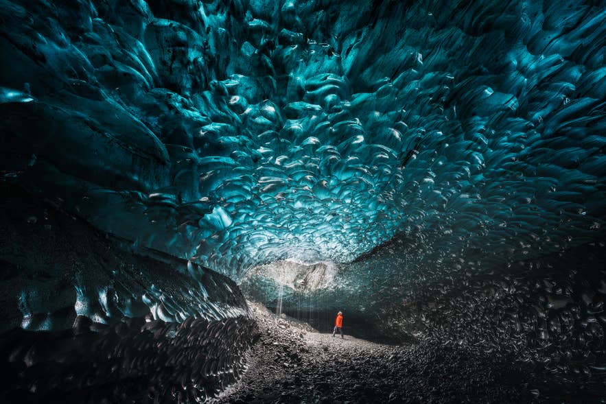 Lone visitor dwarfed by a turquoise ice cave ceiling in Iceland on a day when tours could run.