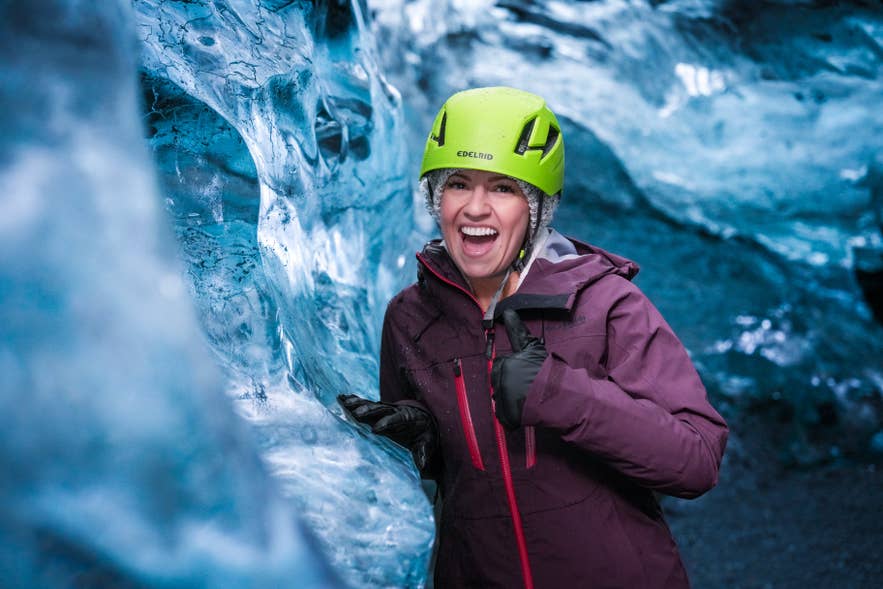 Smiling visitor in a helmet beside a blue ice wall on an Iceland ice cave tour booked for the winter season.
