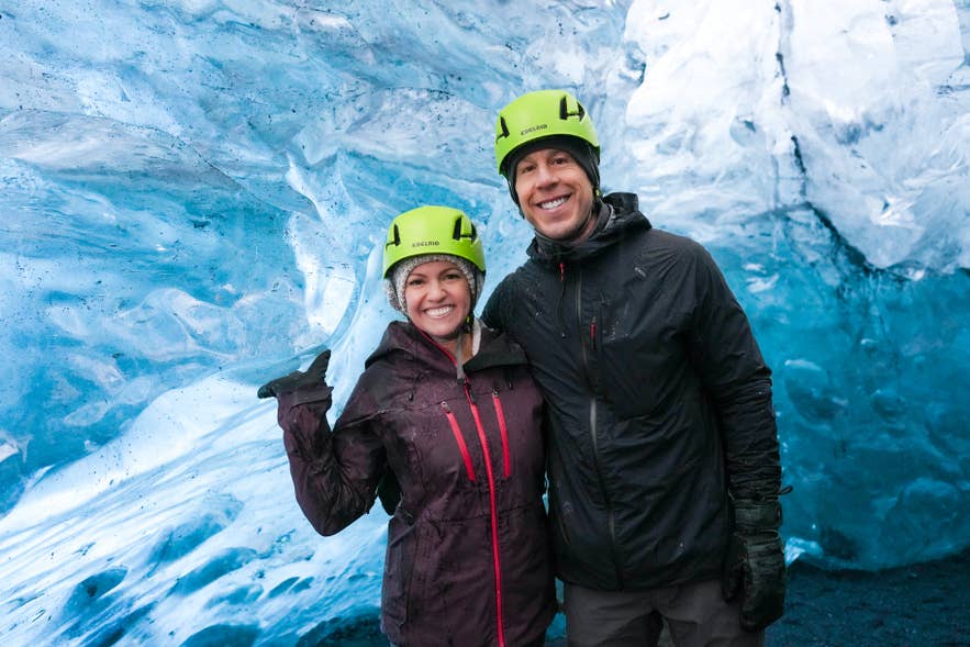Two visitors in helmets smiling inside a blue ice cave, one of the booked tours counted in the study.