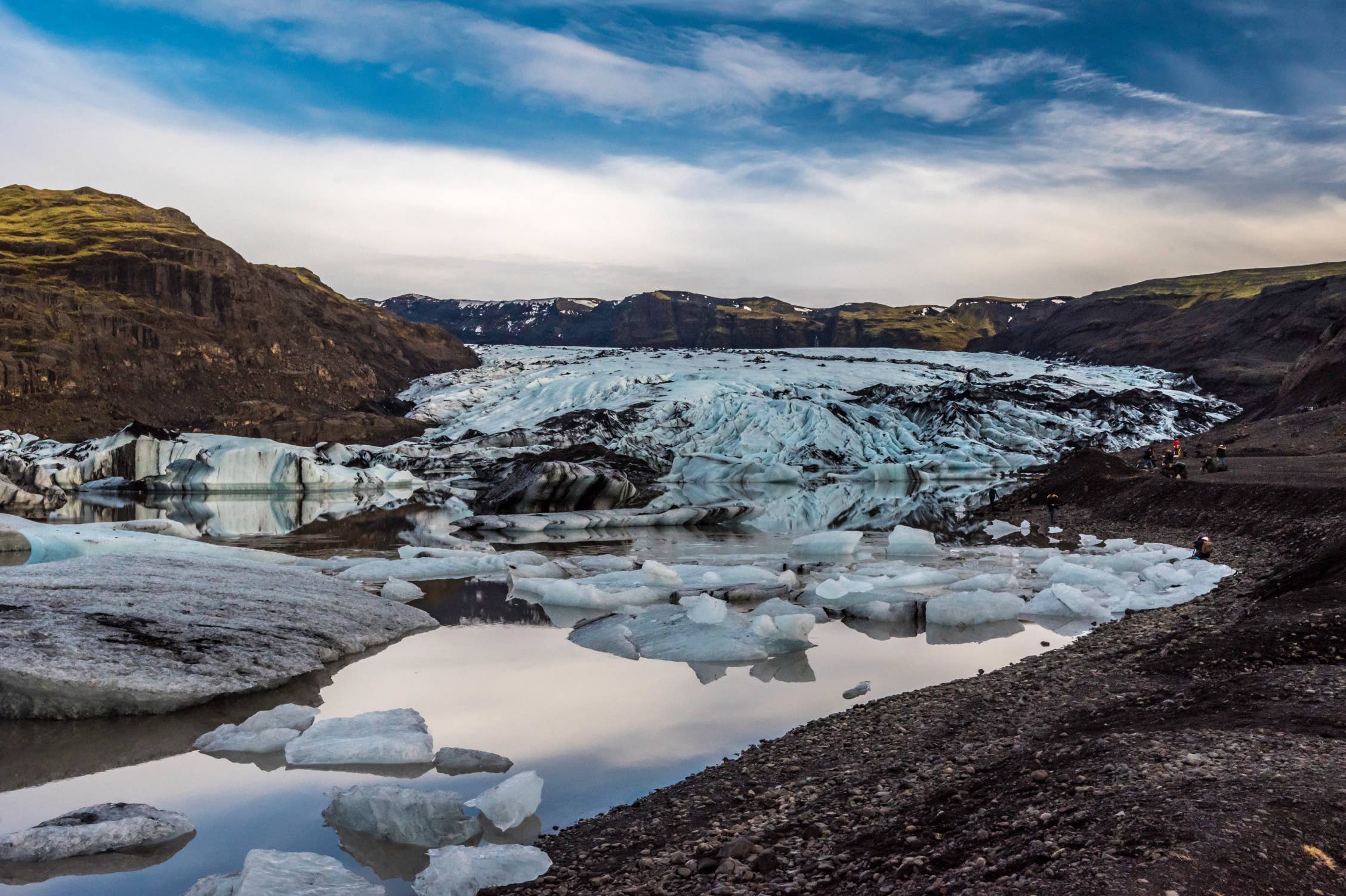 Scattered icebergs float on Solheimajokull Glacier as it stretches between dark volcanic hills.