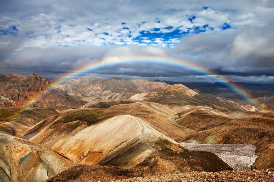 A bright rainbow arcs over the colorful rhyolite hills of Landmannalaugar in the Icelandic Highlands.