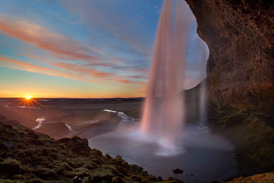 Een zachte zonsondergang verlicht het landschap achter het vallende water van Seljalandsfoss in Zuid-IJsland.