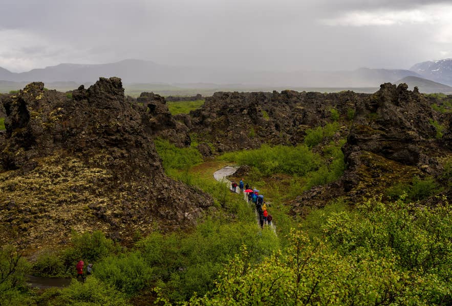 Een groep wandelaars loopt over een pad tussen de donkere lavaformaties van Dimmuborgir in Noord-IJsland.