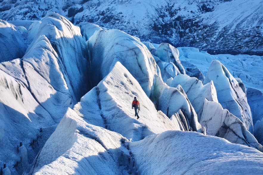 Un randonneur sur glacier marche sur des formations de glace bleue acérées sur le glacier Solheimajokull, dans le sud de l'Islande.