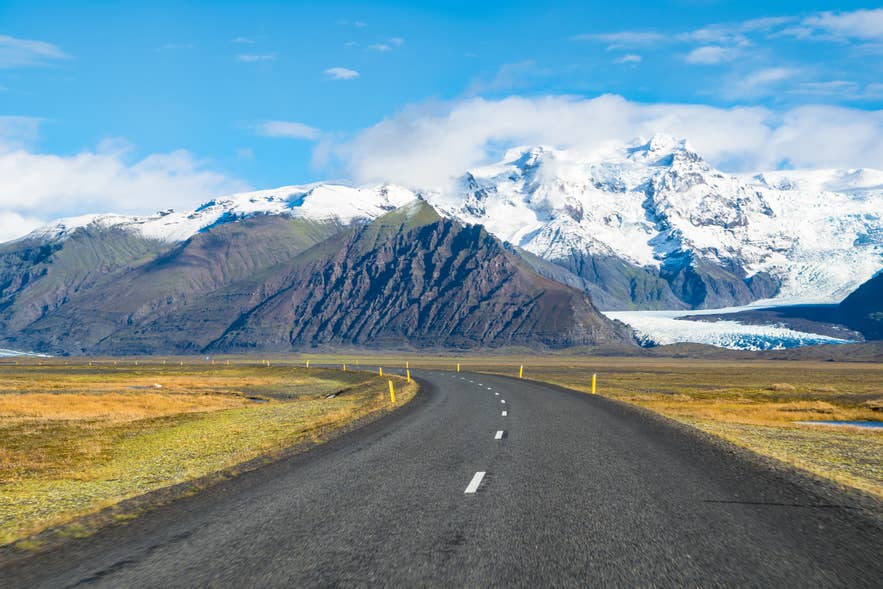 Una strada tortuosa conduce verso Hvannadalshnukur e le cime innevate del Parco Nazionale Vatnajokull in Islanda.