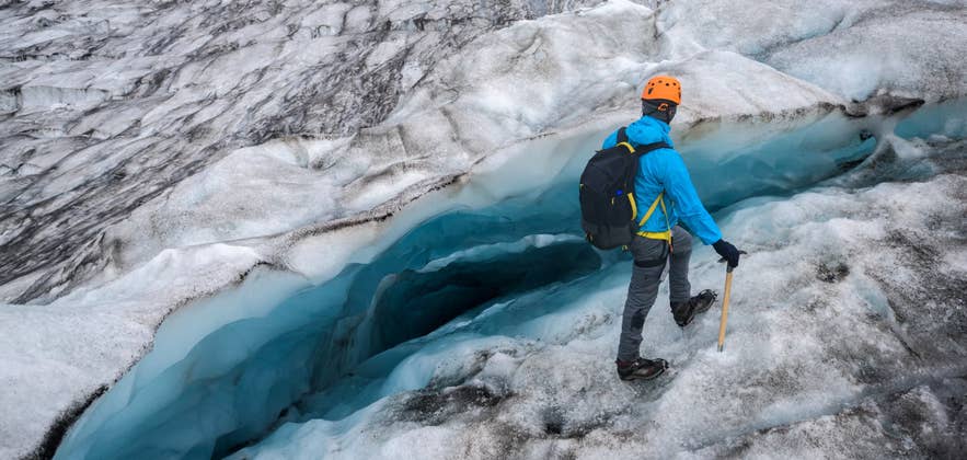 A glacier hiker walks beside a deep blue crevasse on Vatnajokull glacier in Iceland.
