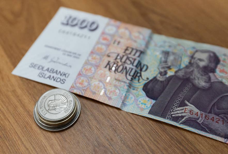 Gestapelte isländische Kronen-Münzen neben einem 1.000-Kronen-Schein zeigen die gängige Währung Islands.