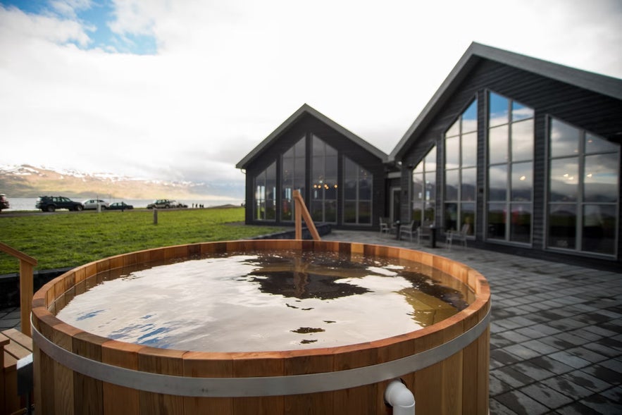 Outdoor wooden hot tub overlooking a fjord and modern lodge at Bjorbodin Beer Spa in Iceland. 