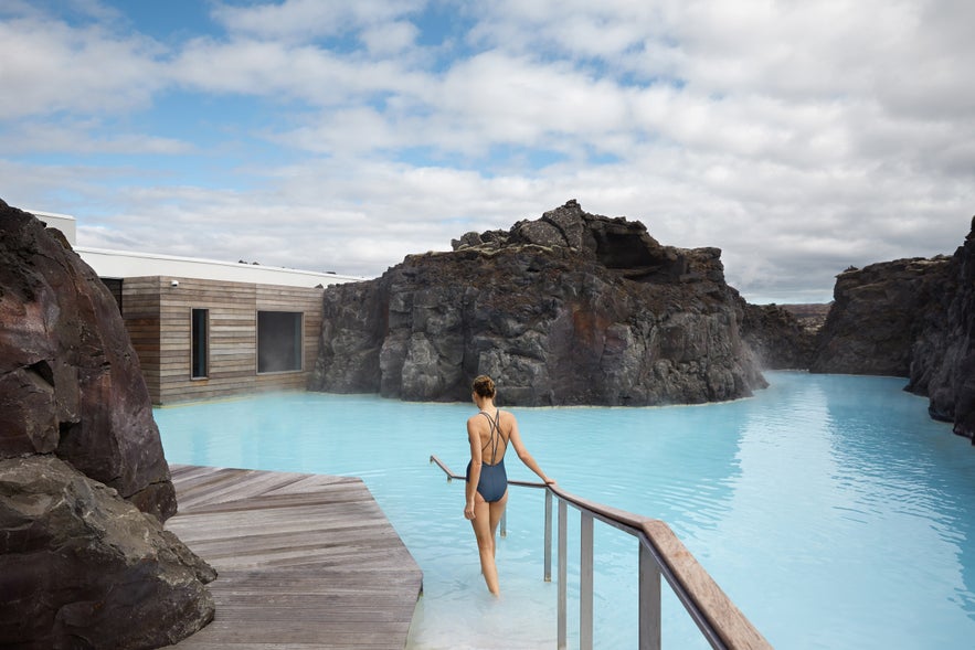 Woman walking into the private milky-blue geothermal lagoon at the Retreat Spa in Iceland.