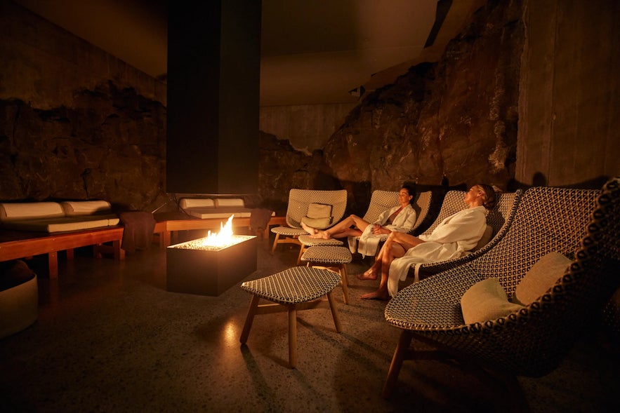 Guests relaxing by a fire in the warm, dimly lit lava-rock lounge at the Retreat Spa in Iceland.