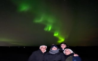 A group of travelers taking a photo with bands of green northern lights in the background.