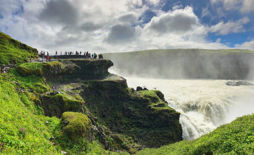 Bezoekers die de Gullfoss-waterval bekijken vanaf een klifplatform aan de Golden Circle in IJsland. Bezoekers die de Gullfoss-waterval bekijken vanaf een klifplatform aan de Golden Circle in IJsland.