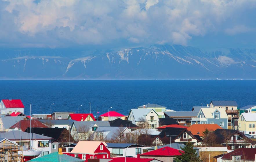 Bunte Häuser in Keflavik auf der Reykjanes-Halbinsel mit schneebedeckten Bergen auf der anderen Seite der Bucht.