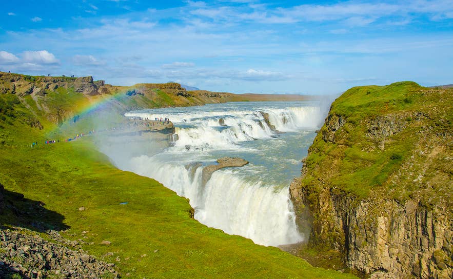 De Gullfoss-waterval in de Golden Circle van IJsland, met krachtige watervallen, groene kliffen van de kloof en een regenboog in de nevel op een zonnige dag. De Gullfoss-waterval in de Golden Circle van IJsland, met krachtige watervallen, groene kliffen van de kloof en een regenboog in de nevel op een zonnige dag.