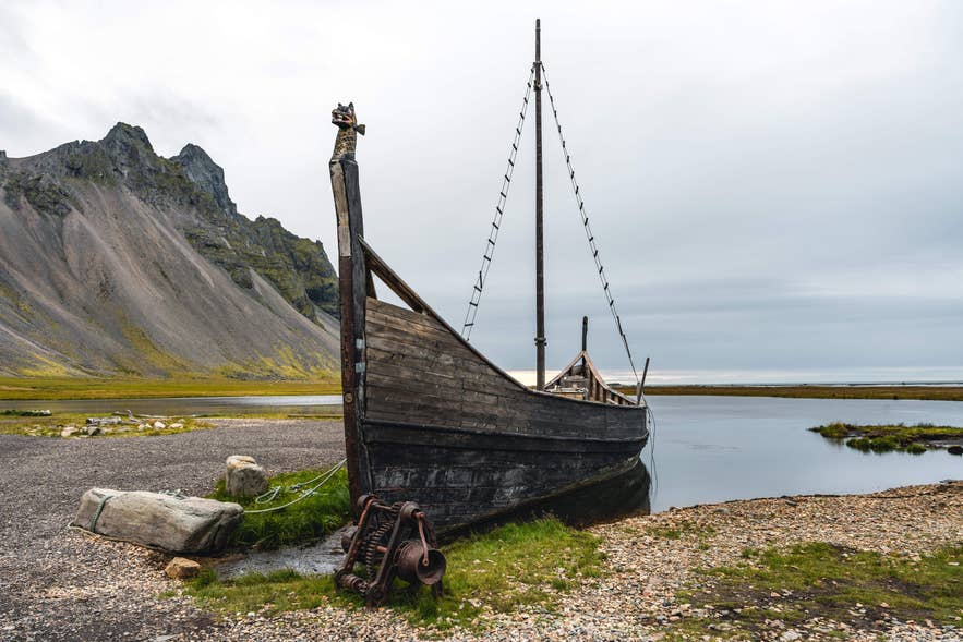 Ein rekonstruiertes Wikingerschiff liegt am Ufer, eingerahmt vom dramatischen Vestrahorn an Islands Küste.