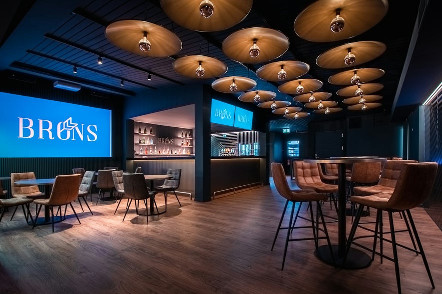 Interior of Brons Keflavík with modern lighting, wood floors, and cozy seating in a stylish nighttime setting. Interior of Brons Keflavík with modern lighting, wood floors, and cozy seating in a stylish nighttime setting.