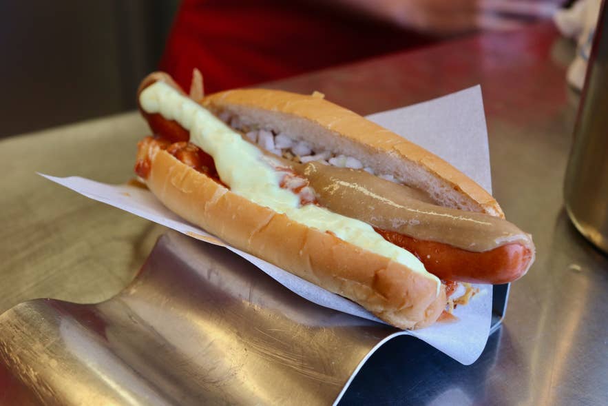 An Icelandic hot dog topped with onions and sauces sits on a counter, ready to serve at a Reykjavik food stand.