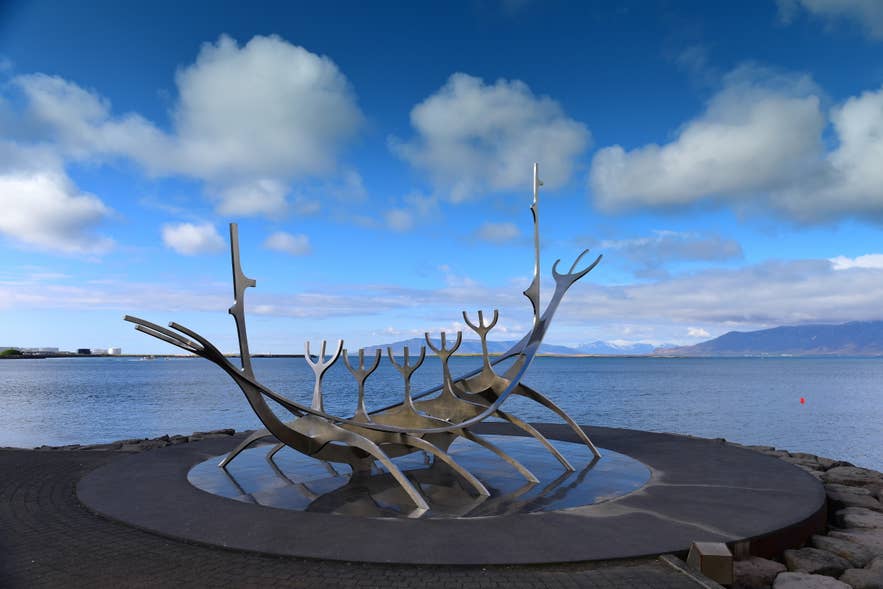ประติมากรรม Sun Voyager ตั้งตระหง่านอยู่ริมน้ำในเมืองเรคยาวิก ภายใต้ท้องฟ้าที่สดใส โดยมีทิวเขาปรากฏให้เห็นอยู่ฝั่งตรงข้ามของอ่าว