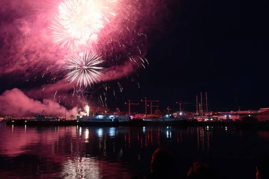 Feuerwerk erleuchtet den Nachthimmel über dem Hafen von Reykjavik während eines Frühlingsfestivals und spiegelt sich im Wasser.