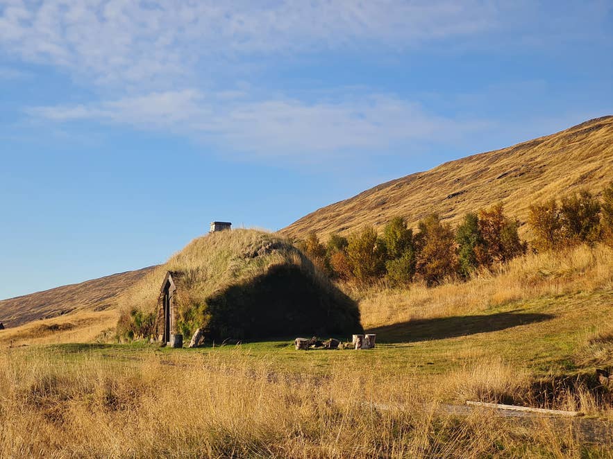 In einem grünen Tal mit Hügeln und Herbstfarben liegt bei Eiriksstadir in Westisland ein mit Gras bedecktes Wikinger-Langhaus.