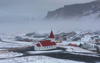 La nieve cubre el pueblo de Vik en la Costa Sur, mostrando casas y la iglesia de techo rojo en la colina.
