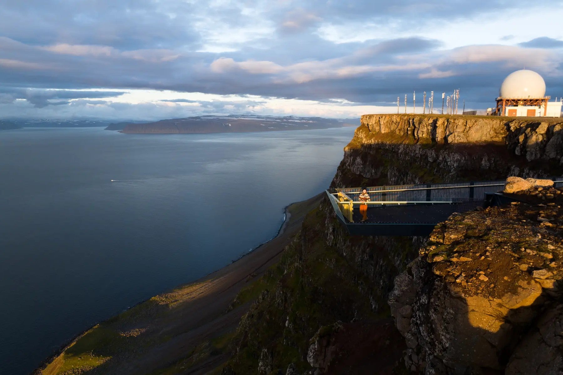 Voyageur admirant la vue depuis la plateforme d'observation de Bolafjall alors que le soleil de minuit se couche sur les Fjords de l'Ouest en Islande.