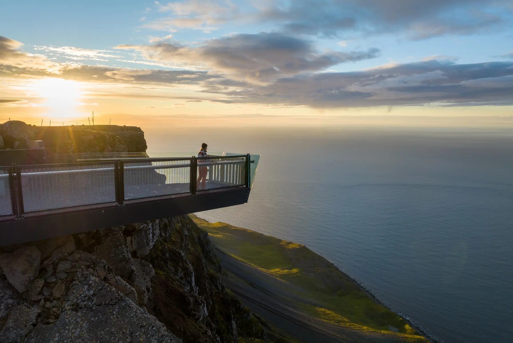 Visiteur debout sur la plateforme vitrée de la passerelle suspendue de Bolafjall surplombant la côte spectaculaire des Fjords de l'Ouest.