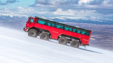 A red monster truck is seen gliding on the ice on top of a glacier.