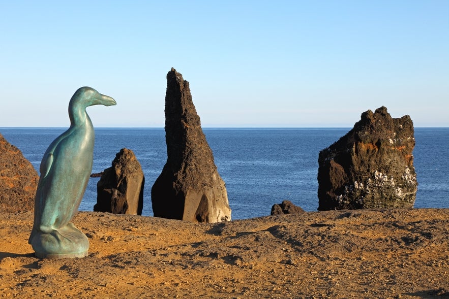 Bronze statue of the extinct Great Auk bird overlooking dramatic sea stacks on the coast of Reykjanes Peninsula.