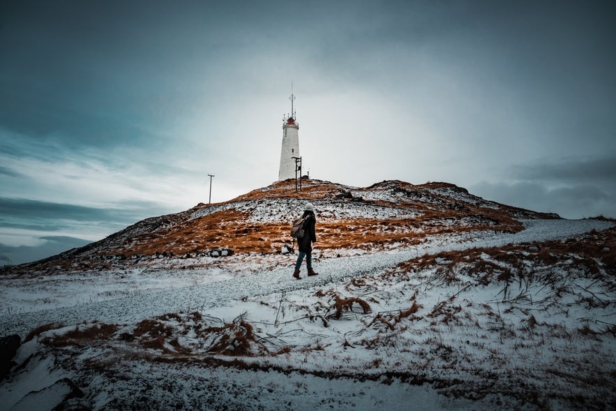 Hiker approaching Reykjanesviti Lighthouse in Iceland on a snowy winter day.