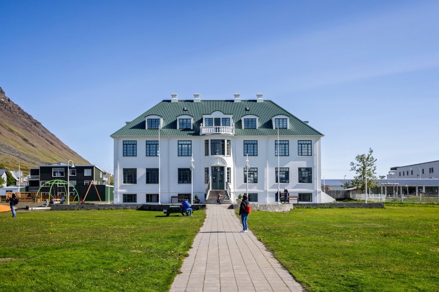 Cultural building in Isafjordur Town Center, Westfjords, with green lawn, walking path, and mountains in the background.