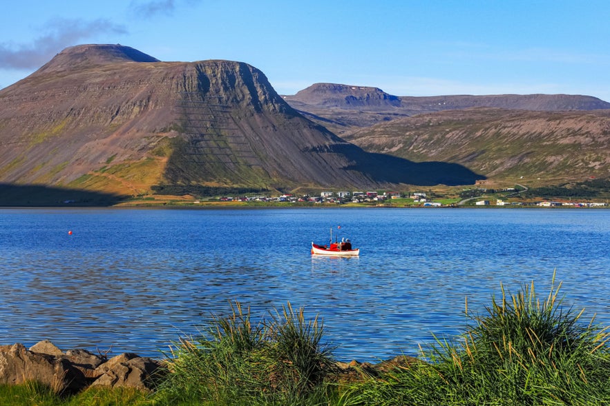 Fishing boat on Isafjordur Fjord with Isafjordur Town and Westfjords Mountains reflected in calm coastal waters.