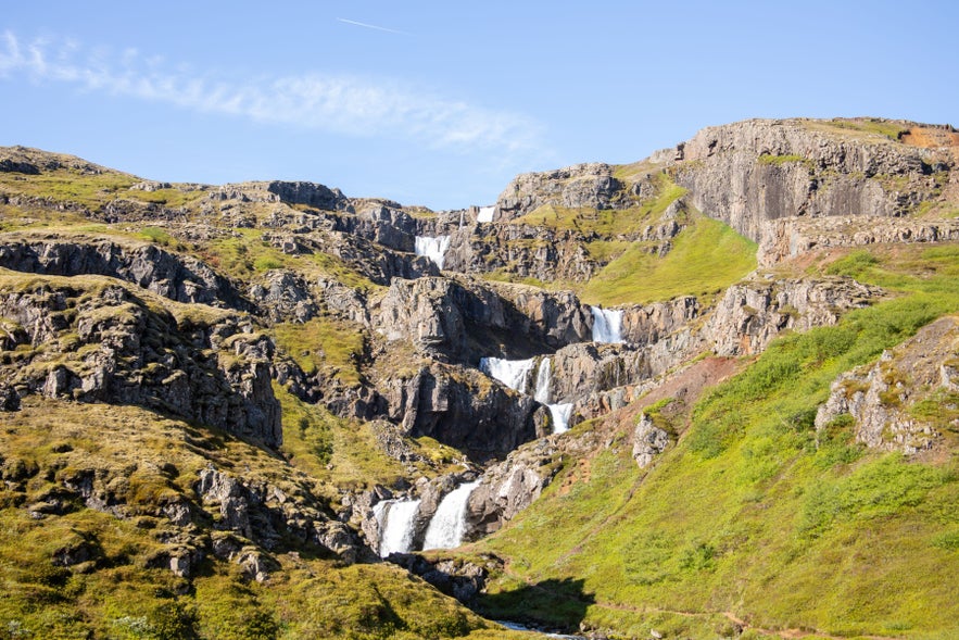 Waterfall near Seydisfjordur in East Iceland, cascading through a rocky valley surrounded by green Eastfjords hills.