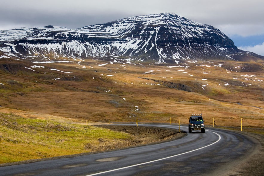 Car driving along Route 93 near Seydisfjordur in East Iceland, with winding road, open highlands, and snow-streaked mountains.